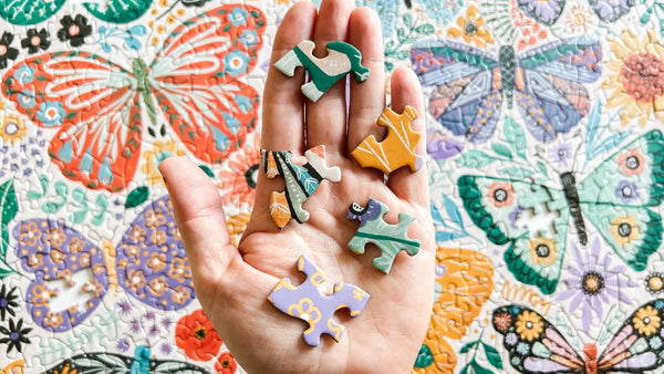 Hand holding colorful puzzle pieces against a floral and butterfly patterned background