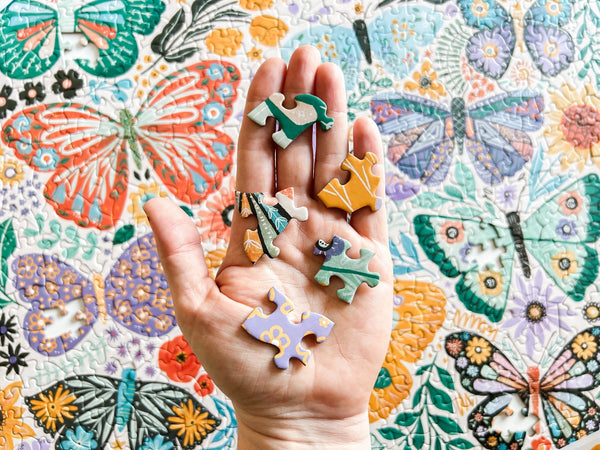 Hand holding colorful puzzle pieces against a floral and butterfly patterned background