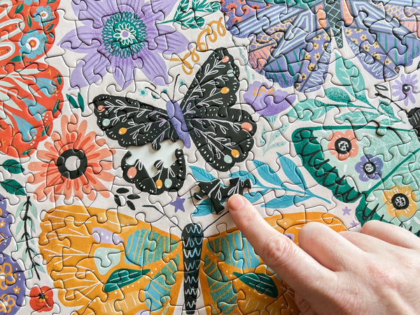 Jigsaw puzzle with a butterfly and floral design, hand placing a piece.