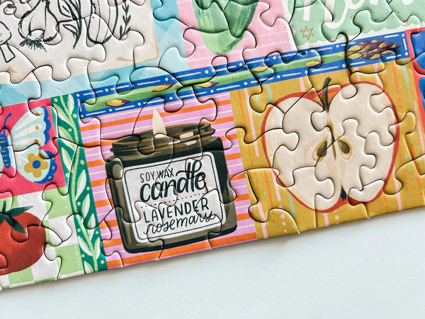 Close up of a colorful puzzle with a soy wax candle and food themed illustrations on a light background