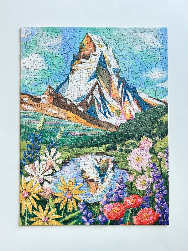 Jigsaw puzzle with artwork of a mountain (the Matterhorn) and floral design on a light blue background