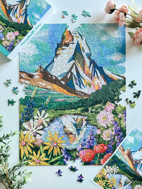 Jigsaw puzzle with art of a floral meadow and lake in front of the Matterhorn on a white surface with flowers around.