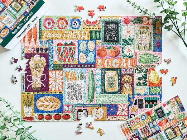 Colorful puzzle with farmers market-themed design on a white surface surrounded by plants and a poster of the puzzle and box lid.