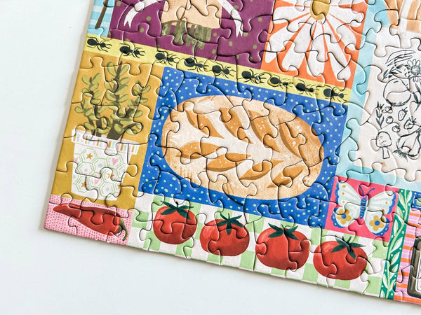 Colorful close up of a section of a puzzle with florals, vegetable and bread illustrations on a white background