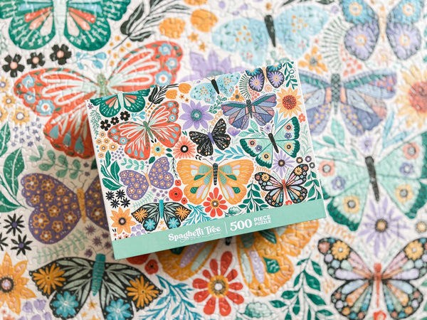 Jigsaw puzzle box with butterfly design on the completed puzzle which is partially blurred.