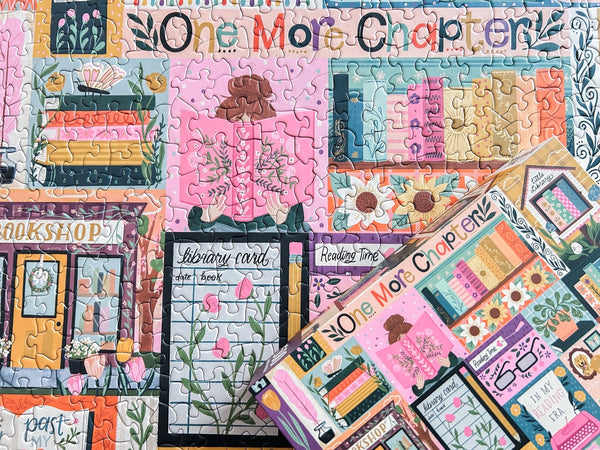 Colorful puzzle box lid with book-themed pieces on top of a completed section showing 'One More Chapter' and a collage of book related art.