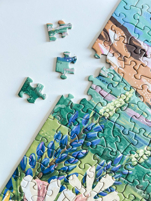 Jigsaw puzzle with a partially completed scene of a floral meadow on a white background. Three puzzle pieces are next to the completed part of the puzzle.