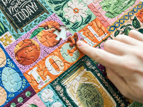 Colorful puzzle with a hand placing a piece, featuring grocery-themed designs.