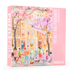 PuzzleFolk 500-piece jigsaw puzzle box titled 'Petals and Pavement', featuring a colorful illustration of a city street scene with pink cherry blossoms, pedestrians, and dogs on a pink background.