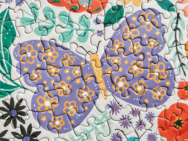 Close up of completed puzzle portion showing a illustration of a butterfly with purple and yellow patterned wings.