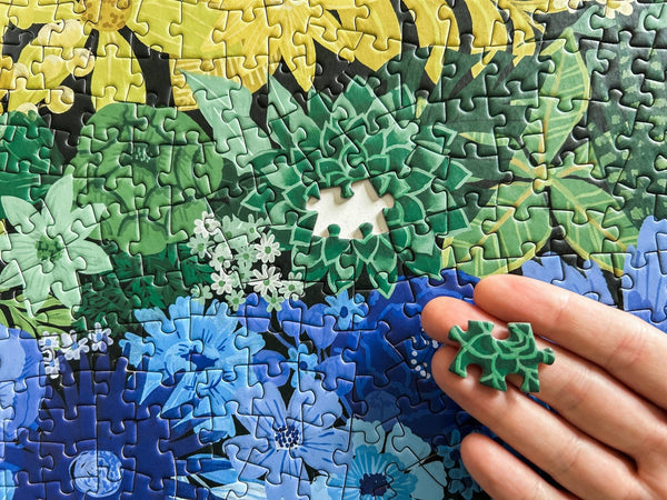 Hand holding a green puzzle piece over a partially completed puzzle with floral patterns.
