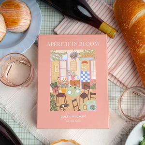 Puzzle box titled 'Apéritif in Bloom' on a table with bread, wine, and pastries.