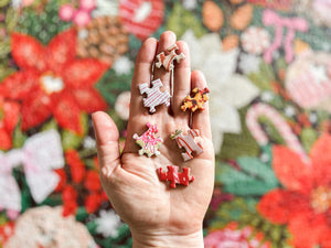 A hand holding several small, colorful Christmas-themed puzzle pieces, over top the completed puzzle shown out of focus.