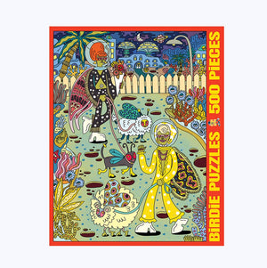 Jigsaw puzzle box against a white surface. Box shows illustration of a two aliens walking their alien pets surrounded by interesting alien houses and plants.