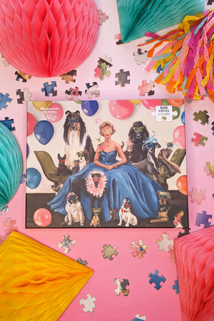 A 500 piece jigsaw puzzle box depicting a whimsical masquerade party scene with a woman on a green couch surrounded by dogs and cats wearing masks.