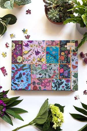 Top view look of a greenbox puzzle box featuring grid collage of illustrated wild flowers separated by gold foil zigzag, surrounded by potted plants and greenery