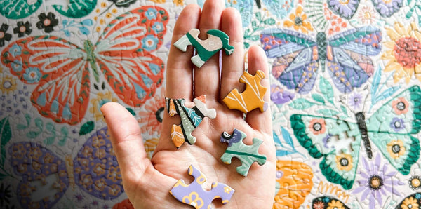 Colorful puzzle pieces held in a hand with a butterfly-patterned background