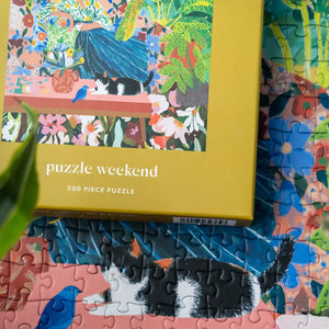 Puzzle weekend 500 piece puzzle with a colorful cat and plant themed design on top of a partially completed puzzle. Photography by Esther Louise