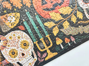A close-up of a completed jigsaw puzzle featuring a colorful Halloween design on a dark background, with a white surface visible along the bottom right corner.