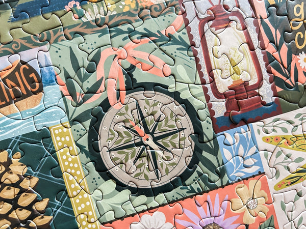 Close-up of a camping themed puzzle with a compass piece and decorative elements.