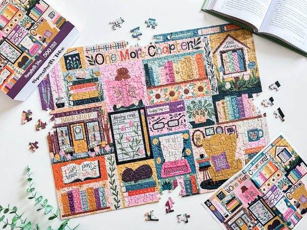 Colorful puzzle with book-themed design on a white surface. Puzzle is mostly completed with a few puzzle pieces scattered nearby. Also visible is an open book, a poster of the puzzle design and the puzzle box lid.