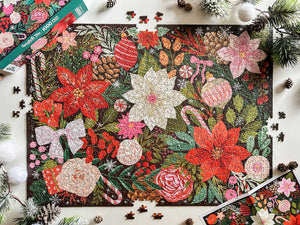 A completed and partially assembled 1000-piece jigsaw puzzle featuring a festive Christmas floral and holiday garland design, styled on a white surface with pine branches, pinecones, and a few loose puzzle pieces.