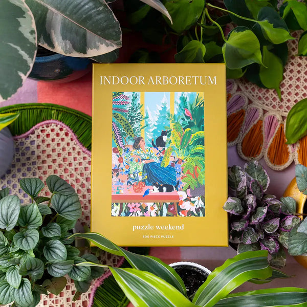 Jigsaw puzzle box titled 'Indoor Arboretum' surrounded by plants. Photography by Esther Louise