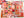 A hand holds an art print featuring a colorful autumn patchwork design with pumpkins, sunflowers, turkeys, leaves, and fall-themed illustrations. The background is a softly blurred mostly completed version of a puzzle featuring the same artwork.