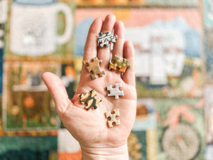 A hand holding several small jigsaw puzzle-piece shaped accessories, with a colorful, blurred background.