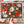 A hand holds a puzzle poster featuring a dense Christmas floral illustration with poinsettias, candy canes, ornaments, pinecones, and snowflakes on a dark background. The print is centered over a blurred view of the completed puzzle.