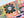 A close-up of a completed jigsaw puzzle featuring a colorful Halloween-themed patchwork design with a large black flower and white skull in the center, surrounded by orange, green, pink, purple, and black sections.