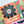 A close-up of a completed jigsaw puzzle featuring a colorful Halloween-themed patchwork design with a large black flower and white skull in the center, surrounded by orange, green, pink, purple, and black sections.