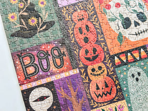 Close up shot of a completed halloween-themed puzzle. Visible art shows a witches hat, pumpkin stack, skull with flowers growing out of it, mummy and ghost with floral design. 