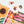 A colorful autumn-themed jigsaw puzzle partially assembled on a white surface, with several loose puzzle pieces scattered above it. The design features a large sunflower, pumpkins, leaves, and a pink scarf in warm orange, yellow, green, and pink tones.