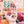 A hand holds several small, colorful, uniquely shaped wooden charms or pendants against a out of focus partial shot of the completed puzzle the pieces come from.