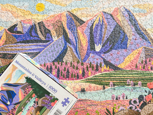 Puzzle box set upon completed version of the puzzle showing illustration of mountain scene.
