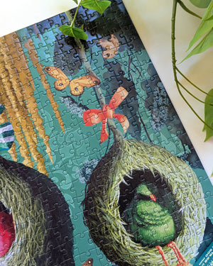 A completed jigsaw puzzle featuring a whimsical illustration of green birds in woven nests, displayed on a white surface with green plant leaves framing the scene.