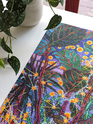 Colorful leaf-patterned fabric on a white surface with a plant in the background