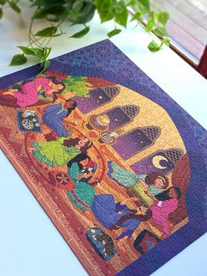 Top view of completed version of the Girls Night puzzle showing an illustration of women chatting and enjoying each others company. On white desk with plants.