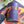 Hand holding a Laila Luxury puzzle box for the puzzle 'Girls Night' shown over portion of the completed puzzle on a white desk with plants.