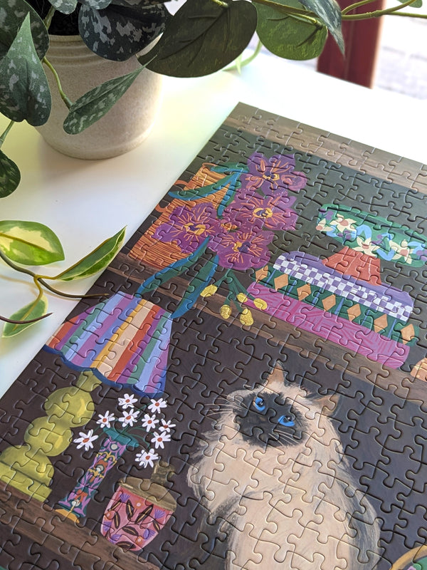 Jigsaw puzzle with a cat and floral design on a table with plants.
