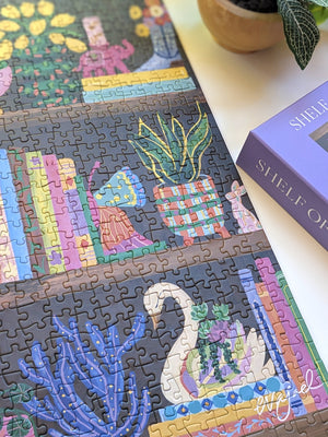 Jigsaw puzzle with a close up of the completed design of a swan planter and books, next to the puzzle box labeled 'Shelf of Whimsy'.