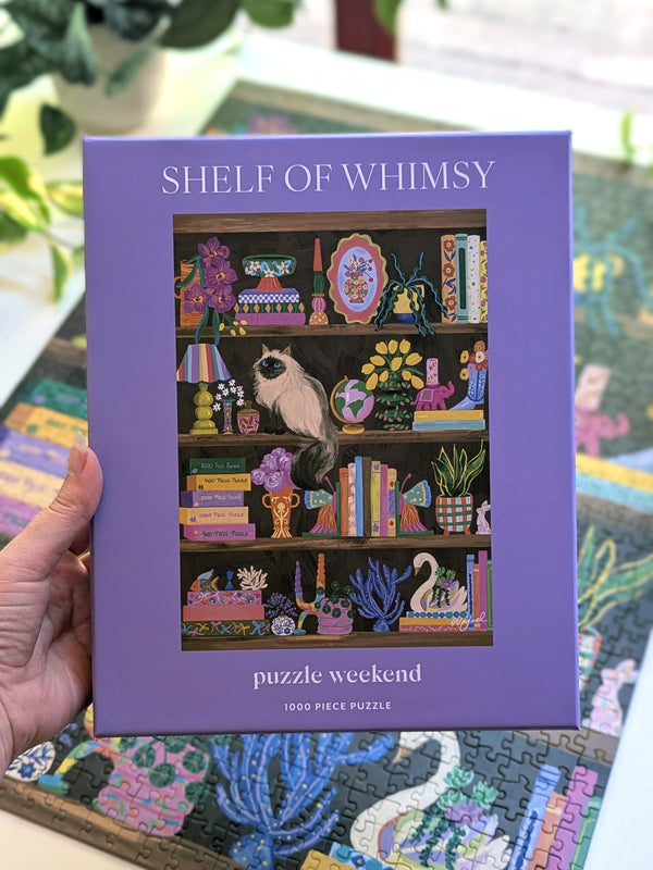 Purple puzzle box titled 'Shelf of Whimsy' held by a hand with a colorful puzzle in the background.