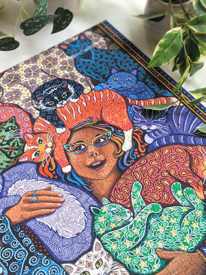 Colorful jigsaw puzzle artwork of a woman with cats and abstract patterns on a desk surrounded by plants