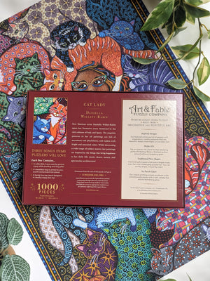 Back of Art & Fable puzzle box showing product details and artist biography. Box is on top of the completed puzzle. 