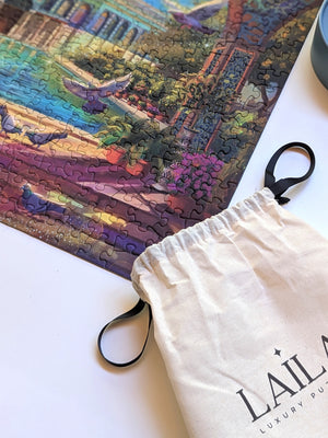 Jigsaw puzzle with a partially completed scene and a branded drawstring bag on a white surface.