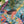A colorful jigsaw puzzle featuring a stylized portrait of a woman with tropical plants, shown in a close-up angled shot with a white surface and green leaves in the background.