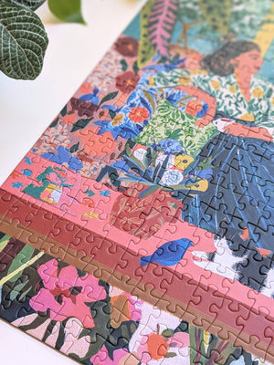 A colorful jigsaw puzzle featuring a whimsical floral and bird illustration, partially assembled on a white surface with a green leaf in the top-left corner.