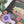Close-up of the corner of a completed puzzle showing flowers and trees. Puzzle is on a white surface near plants.