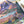 Nearly half of a completed puzzle with  mountain scene artwork is visible on a white surface near plants and the corner of a puzzle box lid.